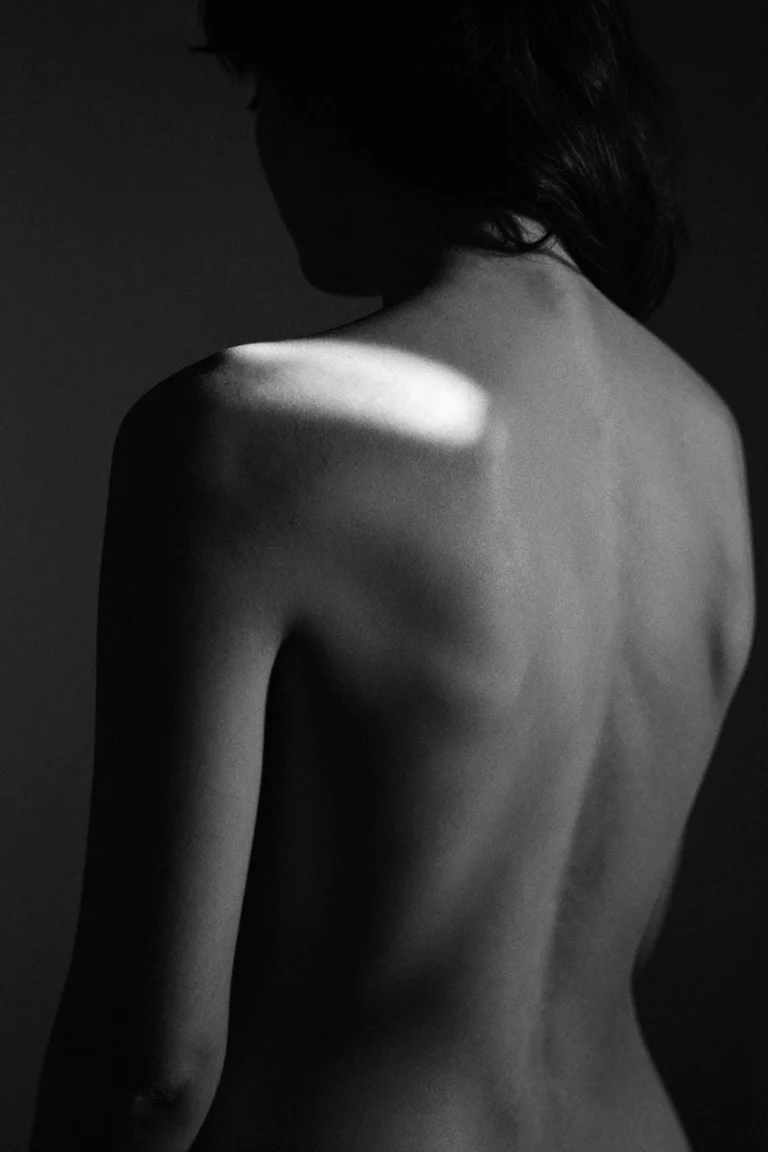 Black-and-white AI study of an adult woman's back crossed by narrow side light.