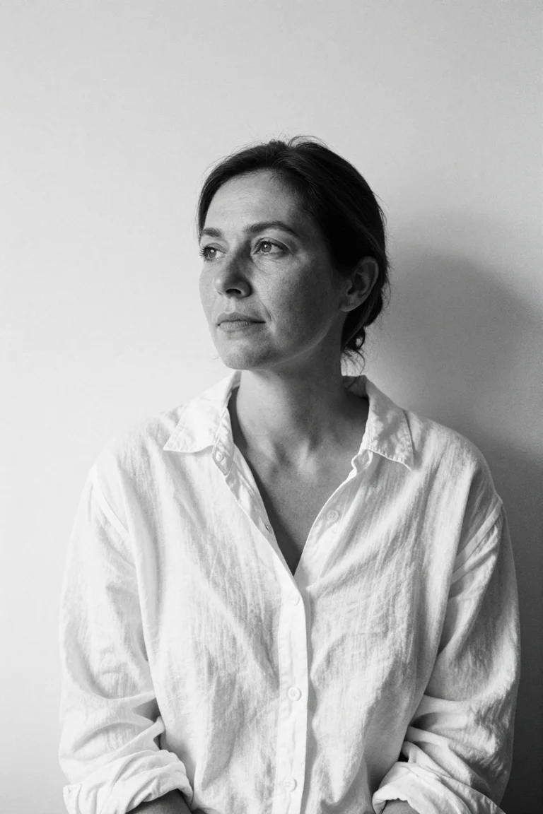 High-key black-and-white AI portrait of an adult woman in a white linen shirt against a pale wall.