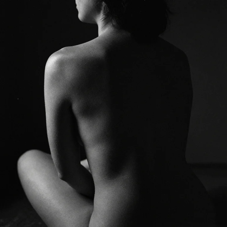 Dark black-and-white AI study of an adult woman's back with light on one shoulder.