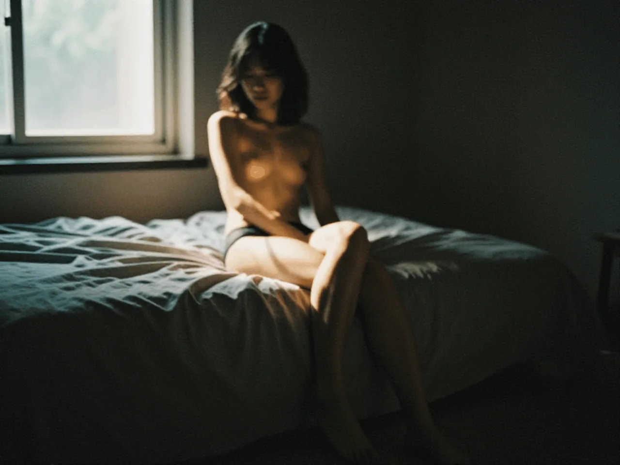 A softly focused portrait of a woman seated on a bed beside a bright window, surrounded by deep shadows
